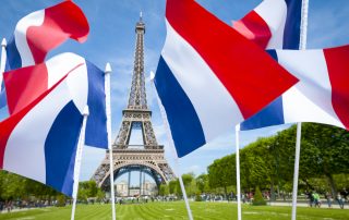 Tricolour French flags flying in front of a bright spring view of the Eiffel Tower in Paris, France