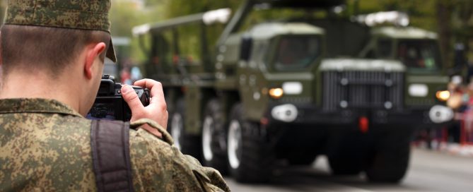 Army journalist photographer. Soldier hold professional camera and takes picture military vehicle
