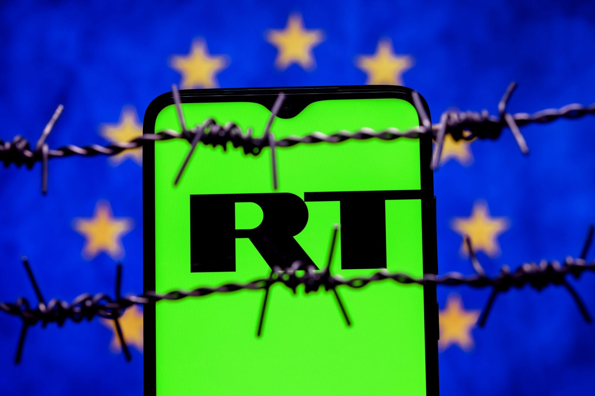 Smartphone with RT (Russia Today) logo on background of flag of European Union behind barbed wire. Russia Today network banning in EU