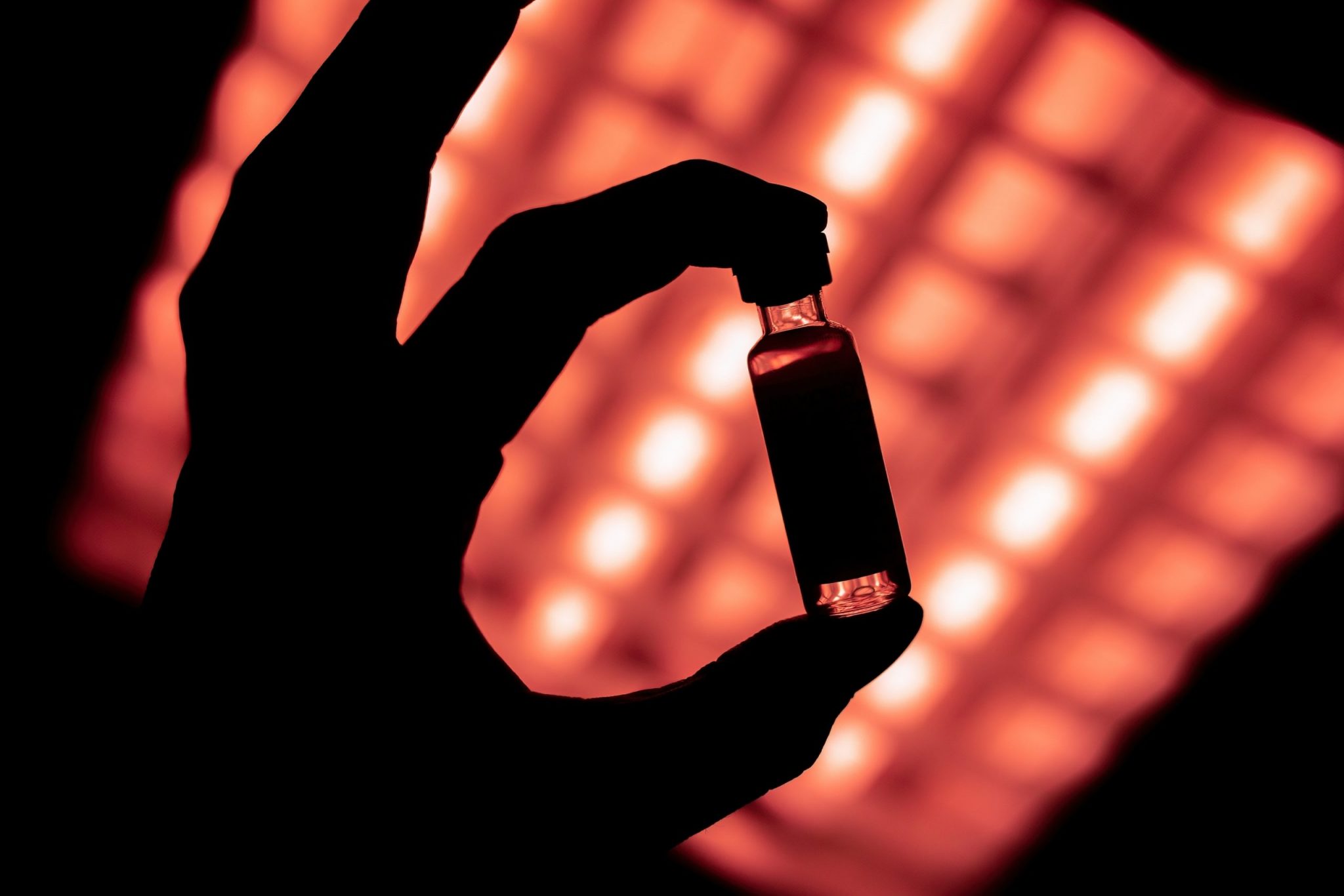 vaccine vial held against red light, showing its black silhouette