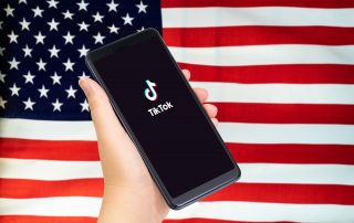 Close up of Hand holding smartphone with TikTok application with US or American flag as background