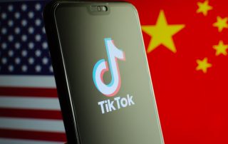 TikTok app logo on a smartphone screen and flags of China and United States on the blurred background.