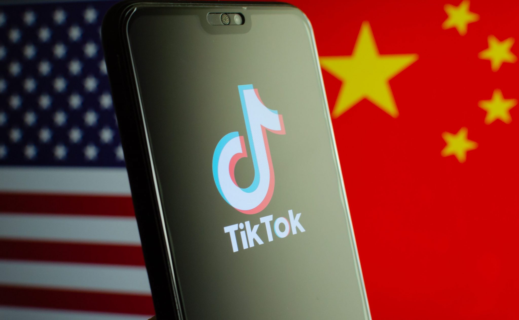 TikTok app logo on a smartphone screen and flags of China and United States on the blurred background.