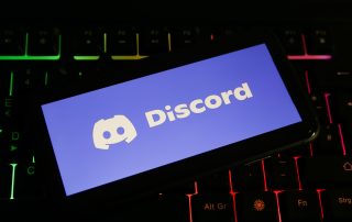 Closeup of mobile phone screen with logo lettering of discord on computer keyboard