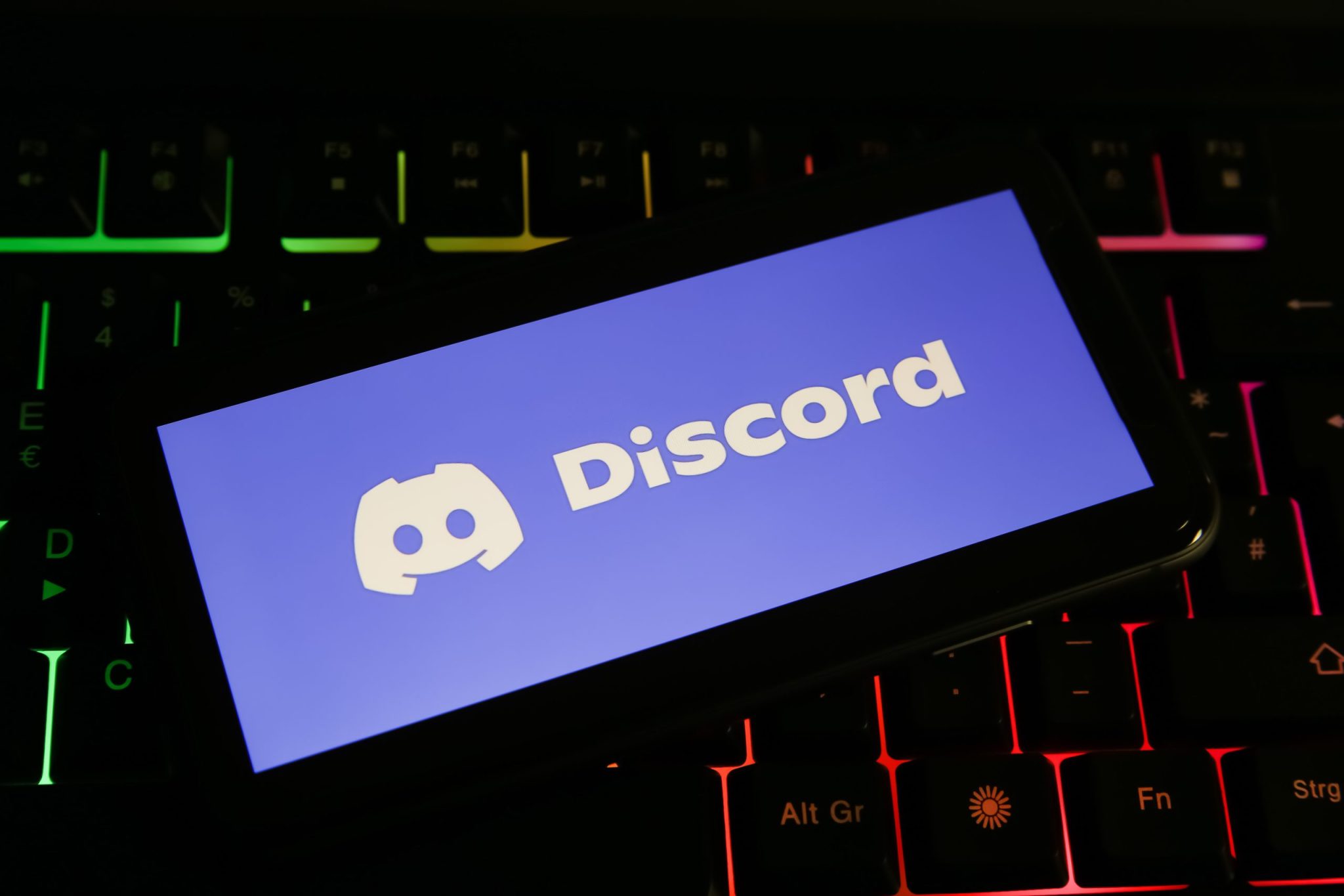 Closeup of mobile phone screen with logo lettering of discord on computer keyboard