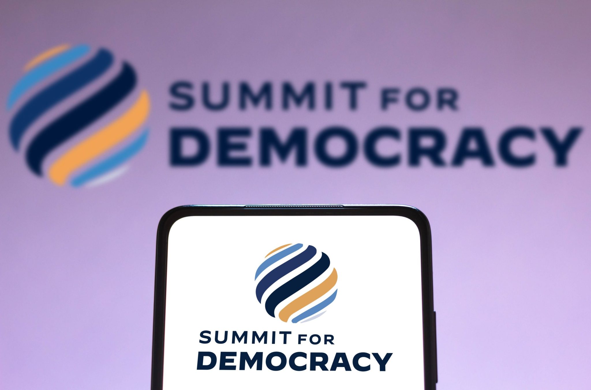 In this photo illustration the Summit for Democracy logo seen displayed on a smartphone and on the background