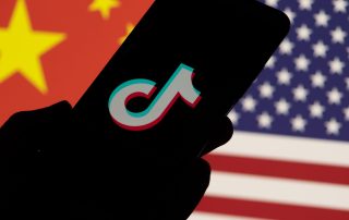Smartphone with TikTok brand logo on screen and USA vs China flag background.