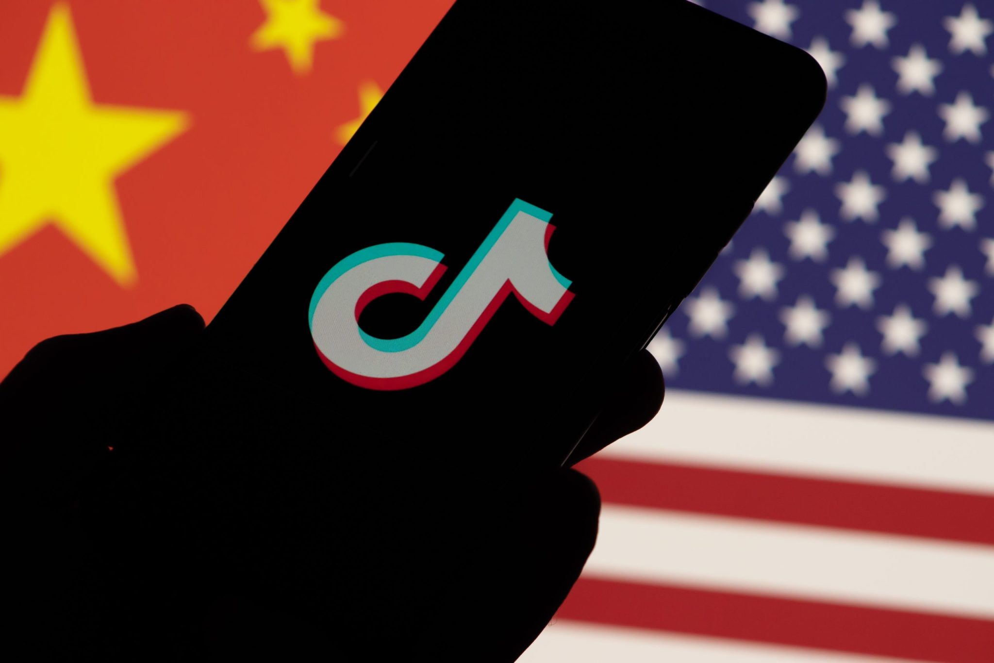 Smartphone with TikTok brand logo on screen and USA vs China flag background.